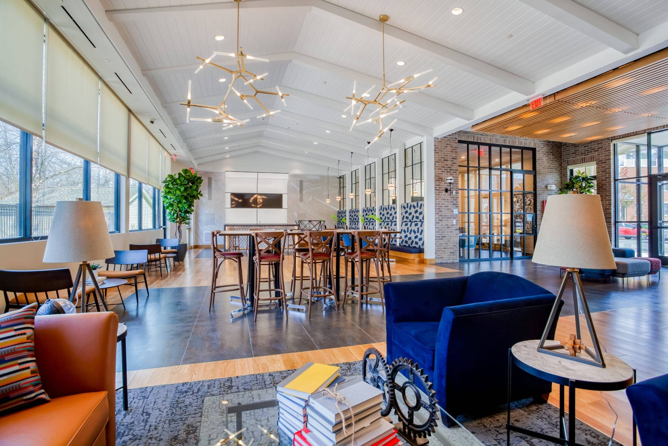 Modern, spacious lounge area at Windsor at Oak Grove with large windows, contemporary light fixtures, comfortable seating, tall tables, potted plants, and decorative accents creates a welcoming and stylish atmosphere.